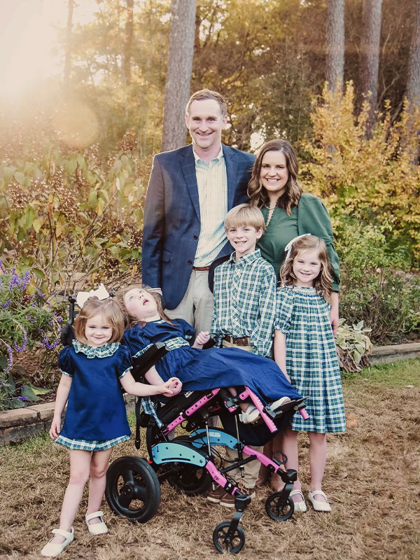 Family portrait outdoors at sunset with two adults and four children wearing coordinated blue and green outfits in a garden.