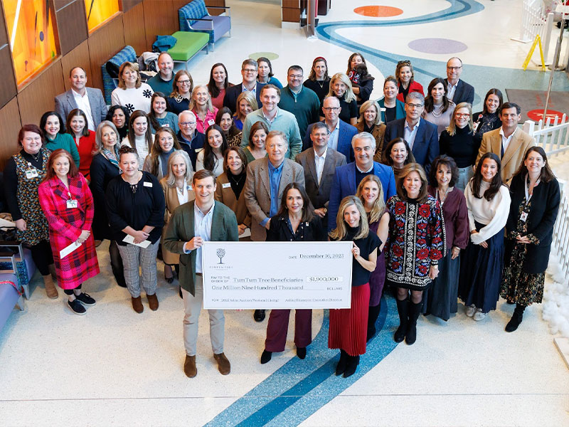 Large group of adults in a bright lobby holding an oversized charity donation check for $1.9 million