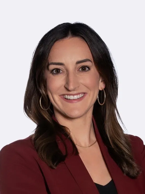 Professional headshot of a woman smiling in a maroon blazer and hoop earrings on a light background