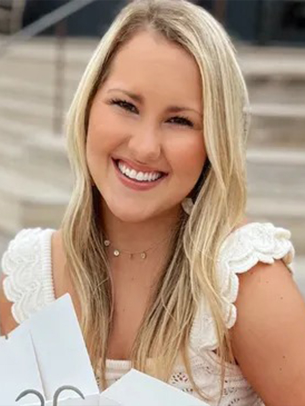 Smiling woman with long blonde hair in white lace top holding shopping bags outdoors on steps