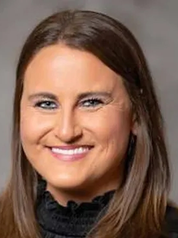 Smiling woman with long brown hair in a black top, professional headshot on a neutral gray background