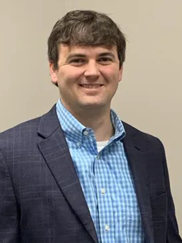 Portrait of a smiling man in a navy blazer and blue checkered shirt on a plain beige background