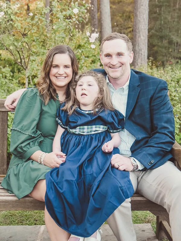 Smiling parents with daughter in blue dress on a garden bench during an outdoor family portrait