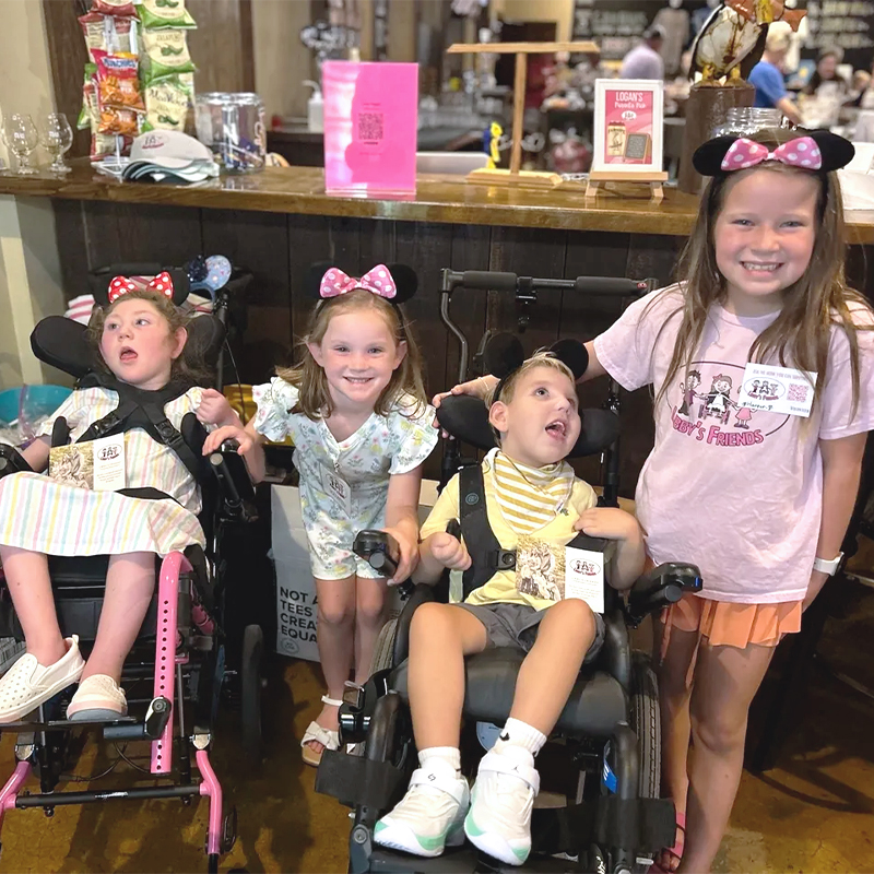 Four children, two using wheelchairs, wearing Minnie ears and smiling at a shop counter during a family outing.