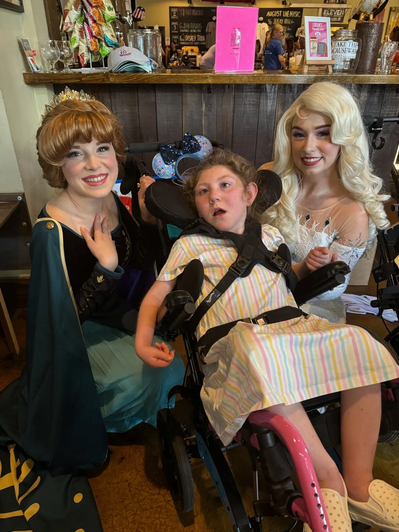 Frozen princesses Anna and Elsa pose with a child in a wheelchair at a cafe.