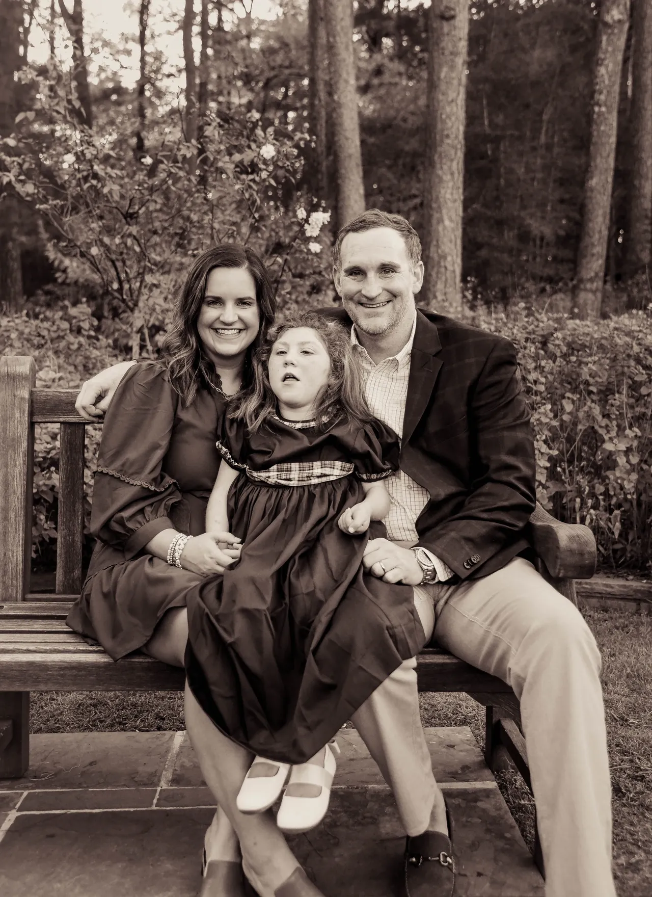 Smiling parents and child seated on a park bench, outdoor family portrait in a garden, sepia tone.