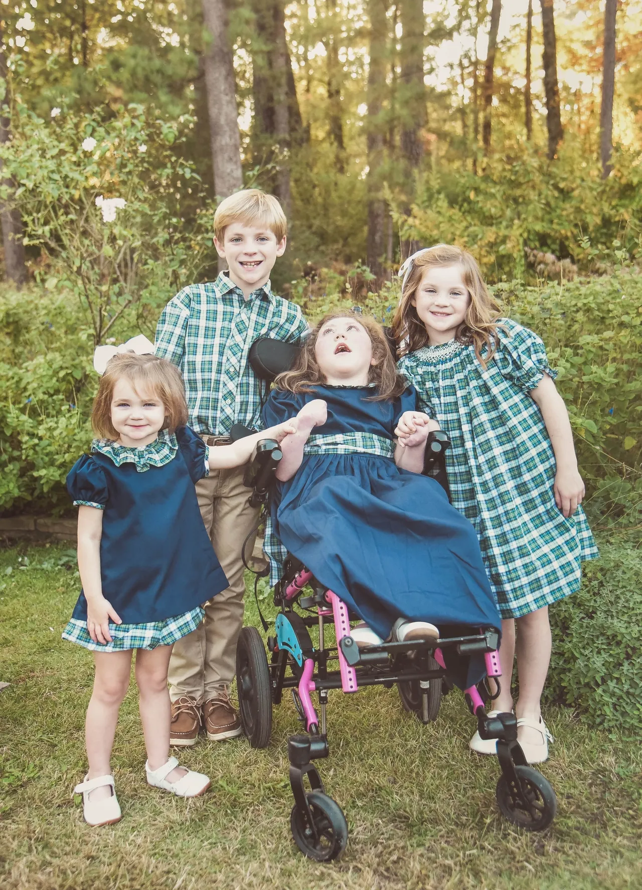 Four siblings smiling outdoors in blue and green plaid outfits, family portrait in a garden.