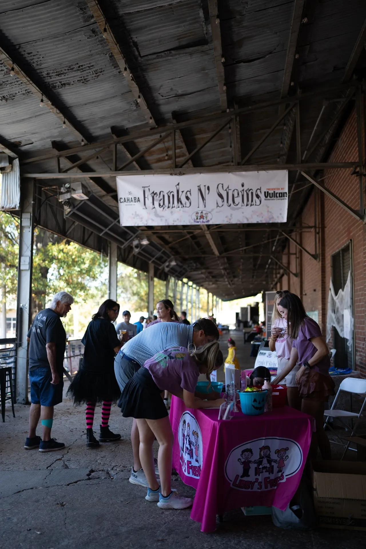 People at Franks N' Steins event at Cahaba Brewing, signing up at Libby's Friends table under covered patio.