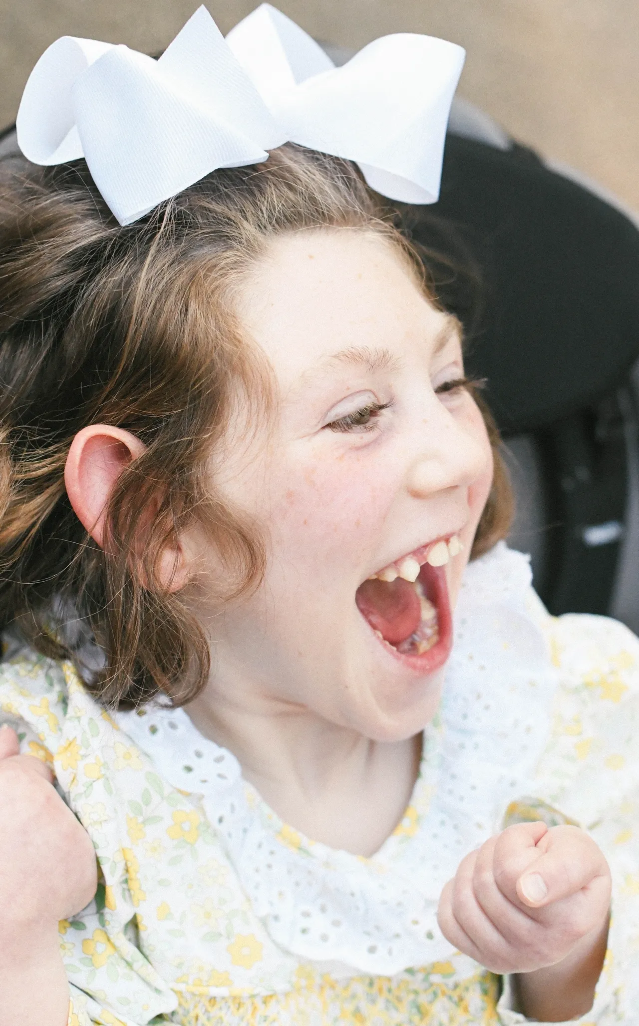 Happy child laughing with a white hair bow and yellow floral dress, close-up