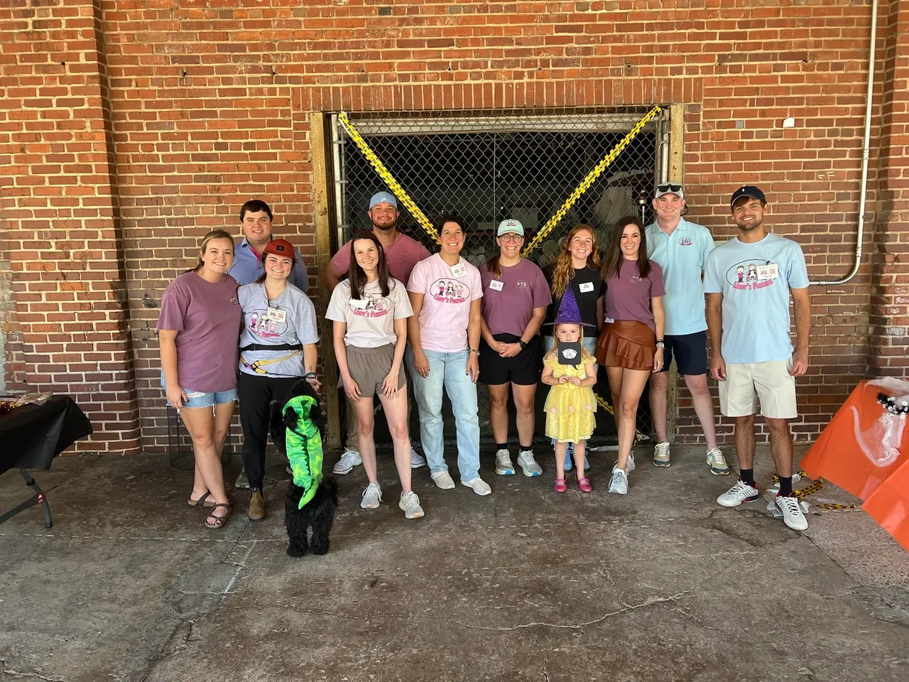 Group photo by a brick wall with a child and a dog in costume at a Halloween community event