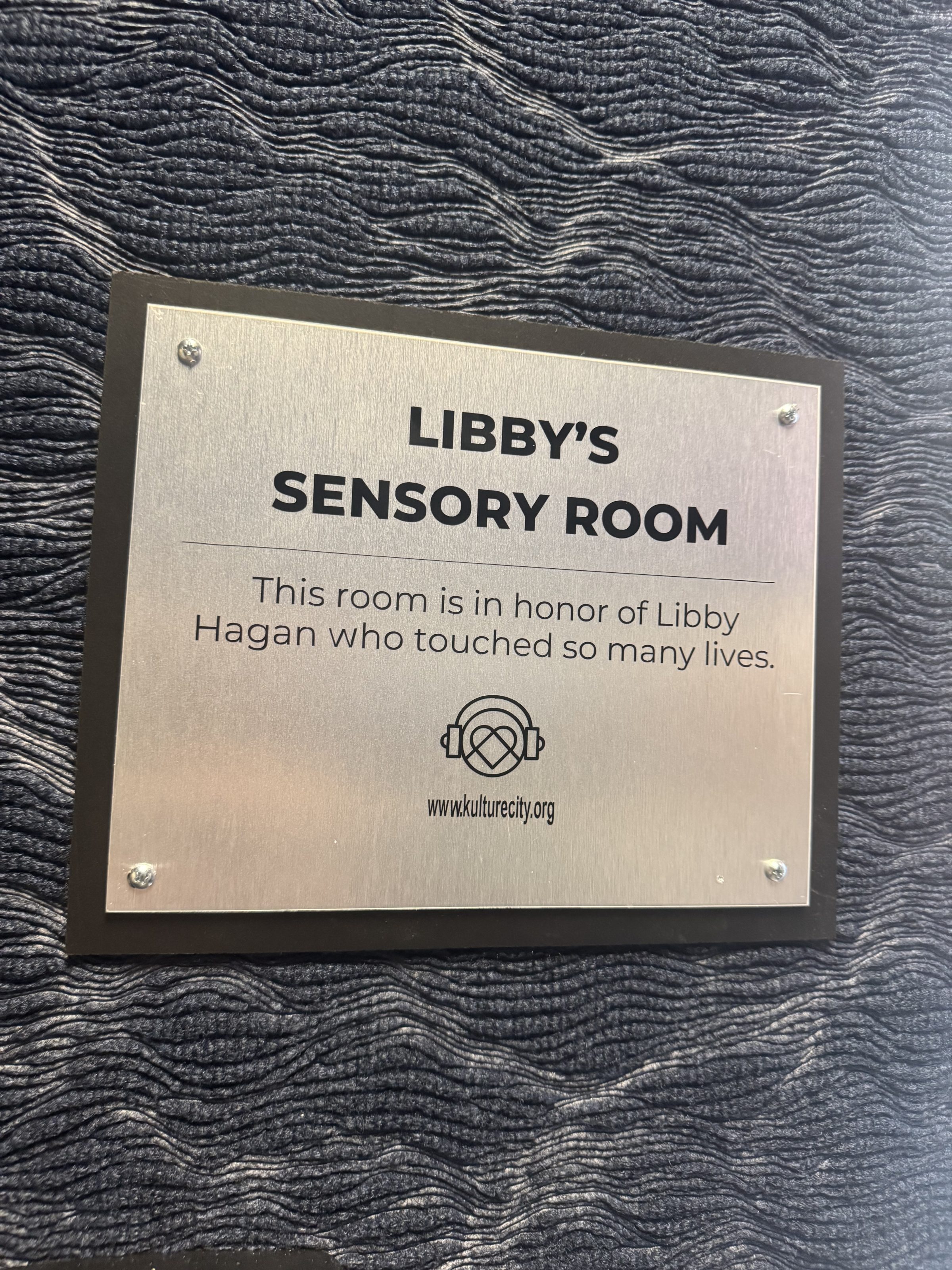 Libby's Sensory Room plaque honoring Libby Hagan, KultureCity sign mounted on textured dark wall.