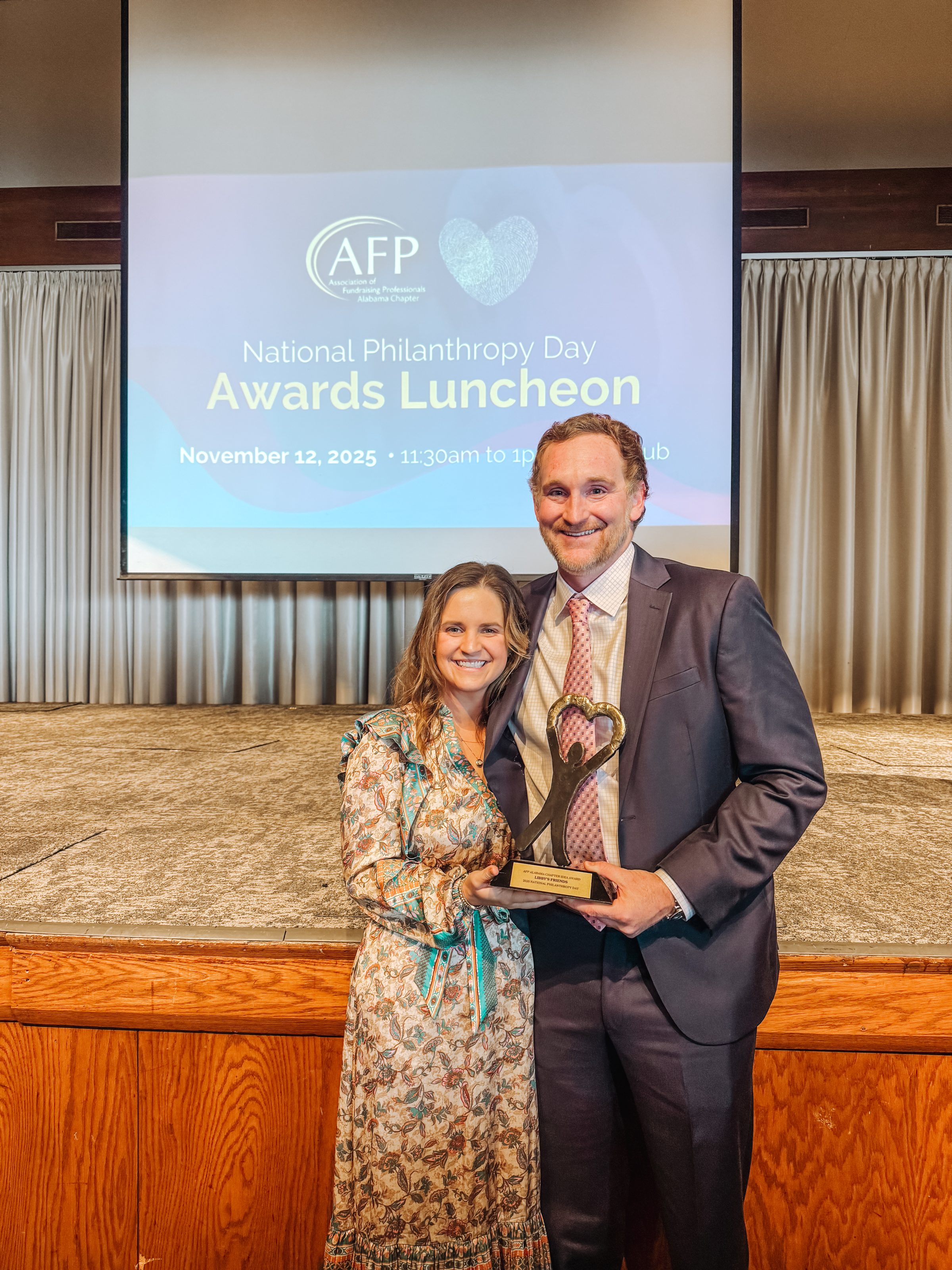 Two award recipients at AFP National Philanthropy Day Awards Luncheon, smiling on stage with trophy.